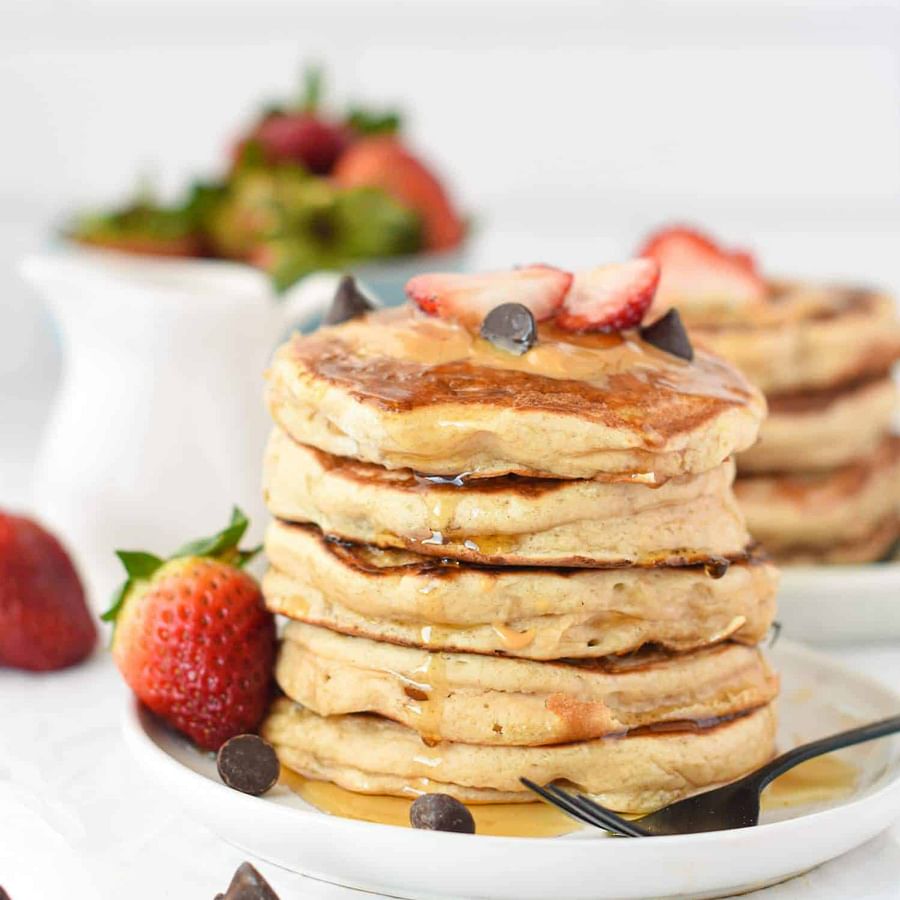 Stack of protein-packed vegan pancakes served with fresh fruits and syrup